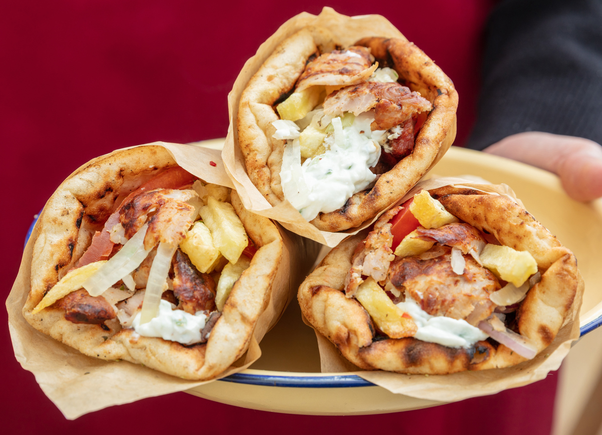 Three freshly made Greek gyros wraps filled with grilled meat, fries, onions, and tzatziki sauce