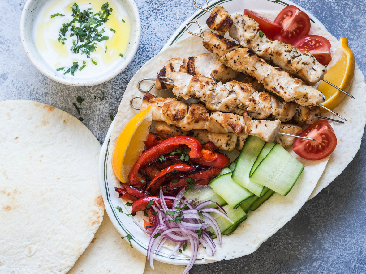 Grilled chicken on metal skewers with of fresh vegetables on the pita and Greek sauce in a bowl