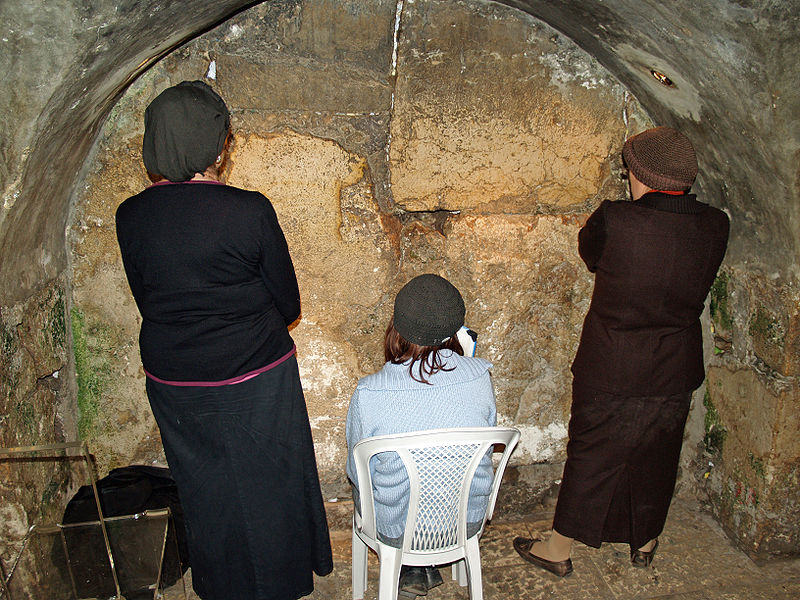 three women facing an arched stone wall