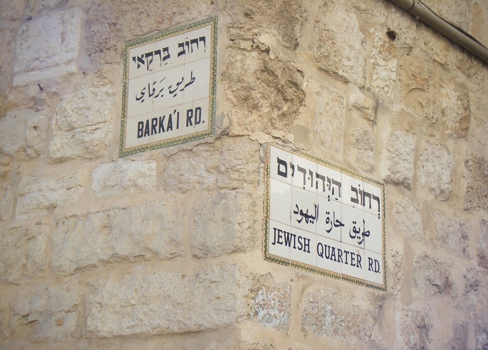 two signs on the stone wall written in Jewish, Arabic and Englsih