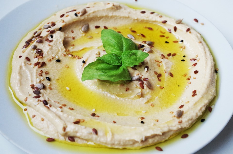 a plate of hummus with olive oil, topped with toasted sesame seeds and basil