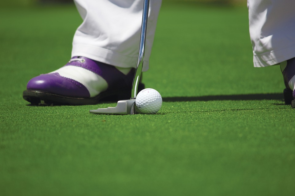 white and purple golf shoes, golf club and golf ball on a golf course lawn