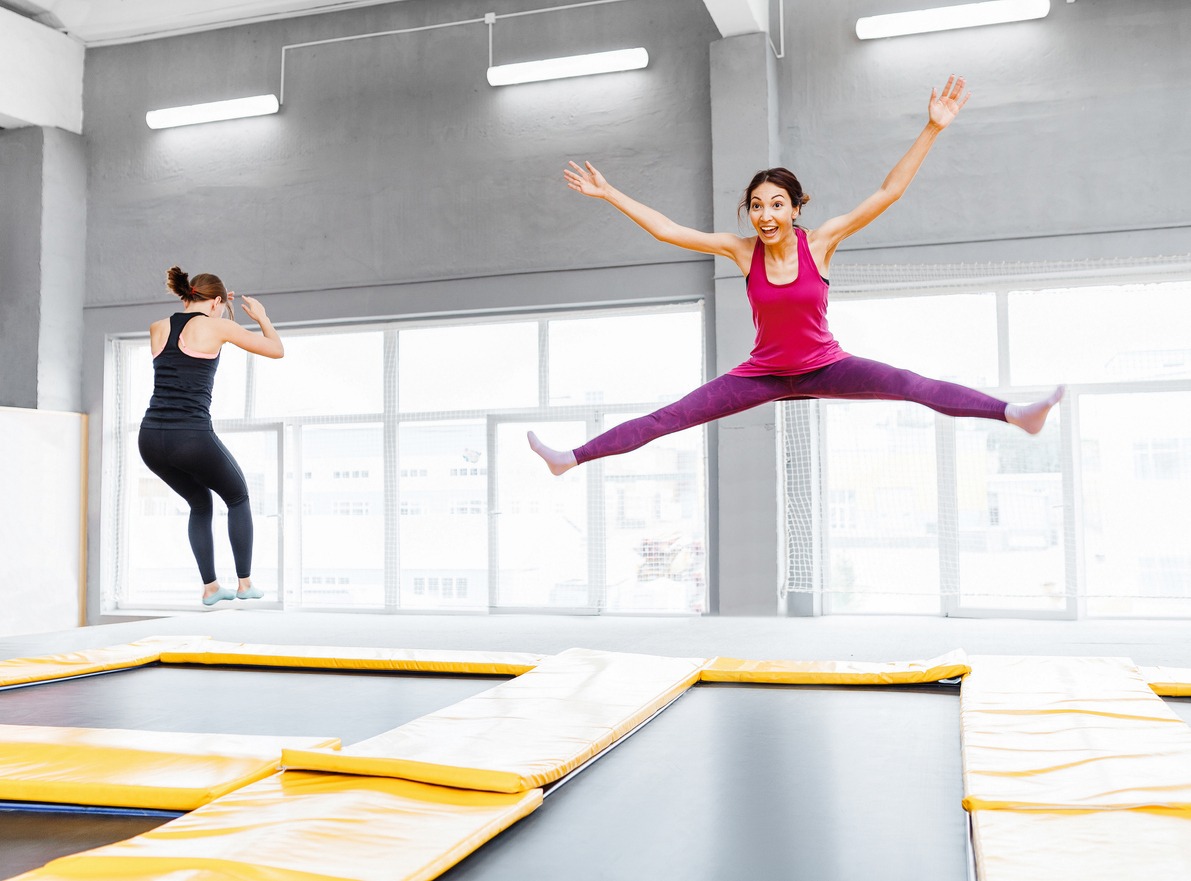 Two young woman friends jumping on a trampoline and doing split indoors